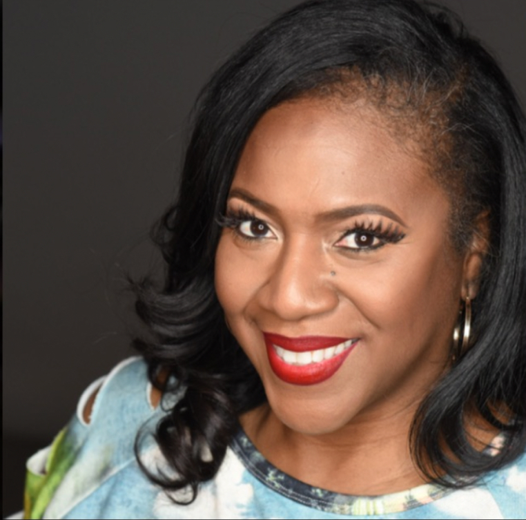 A Black woman is positioned to the right of center, with straight hair curled at the end and smiling toward the camera. She's wearing a blue and green speckled shirt and gold hoop earrings.